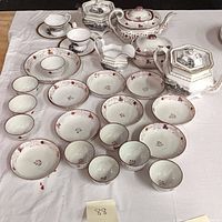 Full set of lusterware china with teapots, cups, saucers, and bowls arranged on white tablecloth.