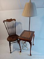 Photo showing vintage wooden chair with curved spindled back and wooden seat next to a wooden side table with cabriole legs and built-in lamp with pleated shade