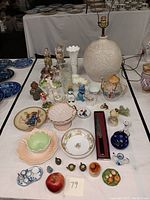 Wide shot showing large ceramic lamp, various figurines, vases, bowls, plates, teapot, and small decorative items on table.