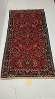 Full view of a rectangular Persian area rug with red background, traditional floral and geometric pattern and black border.