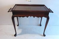 Front view of Queen Anne tea table with extensions pushed in; shows scalloped apron, cabriole legs, dark wood finish.