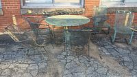 Wrought iron outdoor furniture set including round table and six chairs placed on pavement against brick wall.