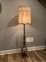 Full height view of antique floor lamp with fabric shade and bronze base on wood floor.
