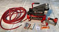 Full lot including air compressor, red air hose, brad nailer, and packages of nails laid out on a cloth surface