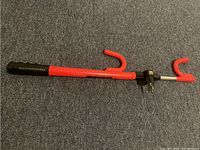 Full view of the red metal steering wheel lock with black grip and red hooks on a blue carpet.