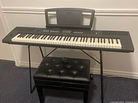 Front view of Yamaha electric keyboard on stand with bench and sheet music holder