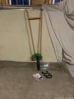 Full view of large Hoss wheel hoe with long wooden handles and large metal wheel against a beige backdrop, showing additional attachments and manual placed on the floor.