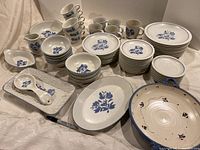 Photo showing full set of ceramic dishes including plates, bowls, cups, mugs, serving platters, spoon, and milk server all featuring a blue floral design