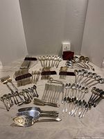 Full layout of the large set of silver silverware items including forks, spoons, spreaders, serving pieces, and four silverware holders with red lining