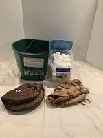 Overall front view of green pitching machine, clear bin of white balls and two gloves