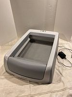 White and gray Petsafe automatic self-cleaning cat litter box with control buttons and power cord visible.