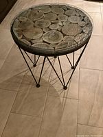 Full view of the small round table showing metal legs and glass top with wood slices underneath