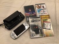 Top view of silver Sony PSP handheld game console with black carrying case and four game cases laid out on a beige surface.