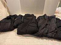 Four pairs of black ski pants and one black ski coat laid out on bed showing styles and sizes.