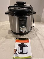 Front view of the Wolfgang Puck pressure cooker with instruction manual.