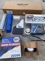 Boxed NAPA ProSelect air filter and other auto parts including valve covers, Edelbrock intake manifold kit, Autocruise cruise control kit, wiper arms.
