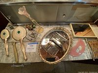Wide top-down view of vanity items on a marble surface showing hand mirrors, brush, glass flower, vintage shavers, tray with shaver parts.