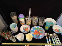 Wide angle showing entire Disney glass and dinnerware collection arranged with plates, bowls, cups, glasses and utensils.