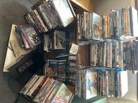 Wide view of DVDs and BluRay movies stacked on a surface along with remote controls and players