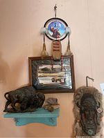 Full view of Native American wall hanging, framed buffalo painting, large buffalo figurine, and two small stone buffalo carvings on blue rustic shelf.