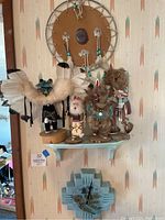 Full view showing five kachina dolls on shelf beneath a large leather and bead suncatcher decorated with feathers, and a turquoise wall clock below.