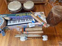 Overview of all instruments showing large drum, bongos, rain sticks, flute, tambourine, Yamaha keyboard in box, and harmonica.
