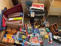 Overall frontal view showing various boxes of pens, pencils, crayons, glue sticks, writing markers, and shredded lubricant sheets on top of the shredder plus plastic storage bins filled with folders and paper.