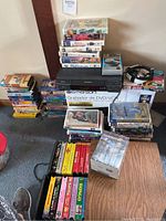 Wide view of the lot showing Magnavox VHS player, Emerson VHS to DVD device box, John Wayne collector series VHS box, and multiple stacks of assorted VHS tapes.