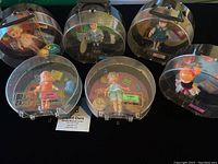 Six Dolly Darlings dolls in round clear plastic cases arranged in two rows