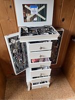Front view of open jewelry box showing top tray, drawers and side panels with hanging necklaces