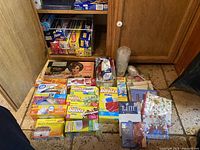 Wide view of the lot showing all boxed items arranged on floor in kitchen environment including Seal-A-Meal box, Basics storage bags, Glad trash bags with Febreze, paper straws, plastic utensils, plastic cups, napkins, and that brand's packaging.