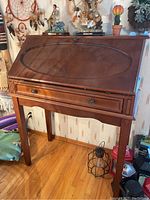 Full view of the vintage solid wood secretary desk showing the closed fold-down front with oval inlay and two drawer pulls below.