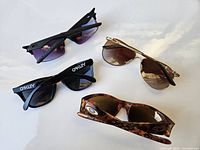 Four Oakley sunglasses with different frame styles and lens colors spread out on a white surface.