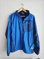 Full front view of blue men's Columbia jacket on hanger with visible tag and chest pocket with zipper.