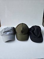 Three hats displayed side by side: gray New Balance, olive green Nobis, and black Lululemon