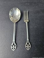 Photo showing front of sterling silver spoon and fork with ornate handles on black background with matchbook for scale.
