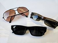 Lot of three sunglasses displayed on white surface, showing overall condition and style.