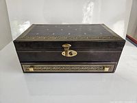 Front view of vintage Mele jewelry box closed, showing dark brown exterior with gold decorative trim and front lock.