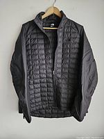 Front view of the black women's jacket hanging on a wooden hanger showing quilted front and smooth sleeves.