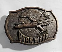 Front side of a metal belt buckle showing a raised X-Wing Fighter from Star Wars and 'STAR WARS' text below it.