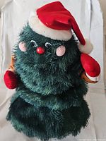 Front view of the animated Christmas tree plush showing facial features, hat, and mittened hands.