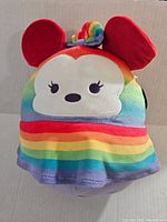 Front view showing face and rainbow striped plush with red ears and unicorn horn.