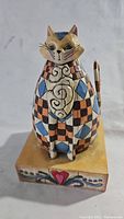 Front view of Jim Shore Abigail Cat Figurine showing geometric blue and orange checkerboard pattern with heart motif on base.
