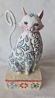 Front view of the hand-painted ceramic cat figure with detailed folk art designs and curled tail.