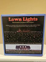 Front of the box showing product name and images illustrating nighttime outdoor decoration with lights illuminating the lawn and house exterior.