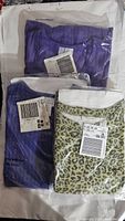 Three new clothing items folded, individually packaged in plastic, in purple shades and leopard print with tags visible.