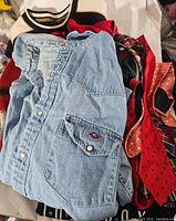 Light blue Painted Mesa denim shirt folded on top of a pile of assorted vintage clothes and ties, showing shirt's details and some ties.