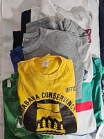 Stack of vintage shirts and sweatshirts showing variety of colors and partially visible graphics.