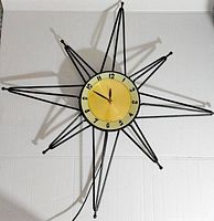 Full view of the starburst wall clock showing metal rays and circular clock face