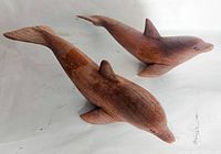 Two carved wooden dolphins viewed from above, showing smooth finish and wood grain.